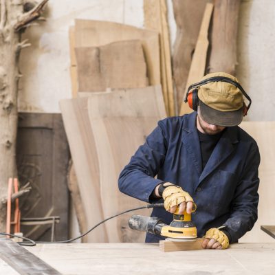 close up male carpenter using electric sander wood